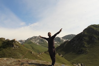 A friendly instructor demonstrating CPR techniques outdoors with mountains and pine trees in the background.