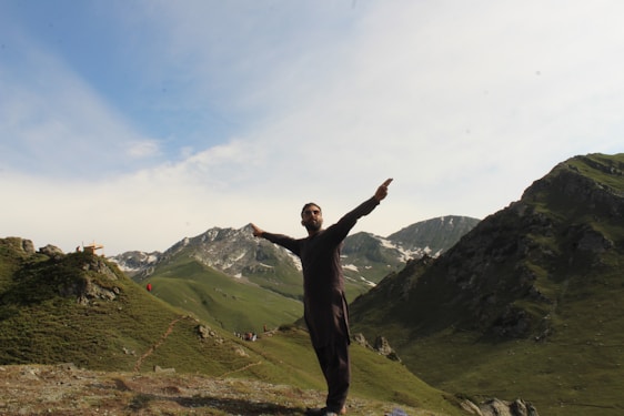 A friendly instructor demonstrating CPR techniques outdoors with mountains and pine trees in the background.