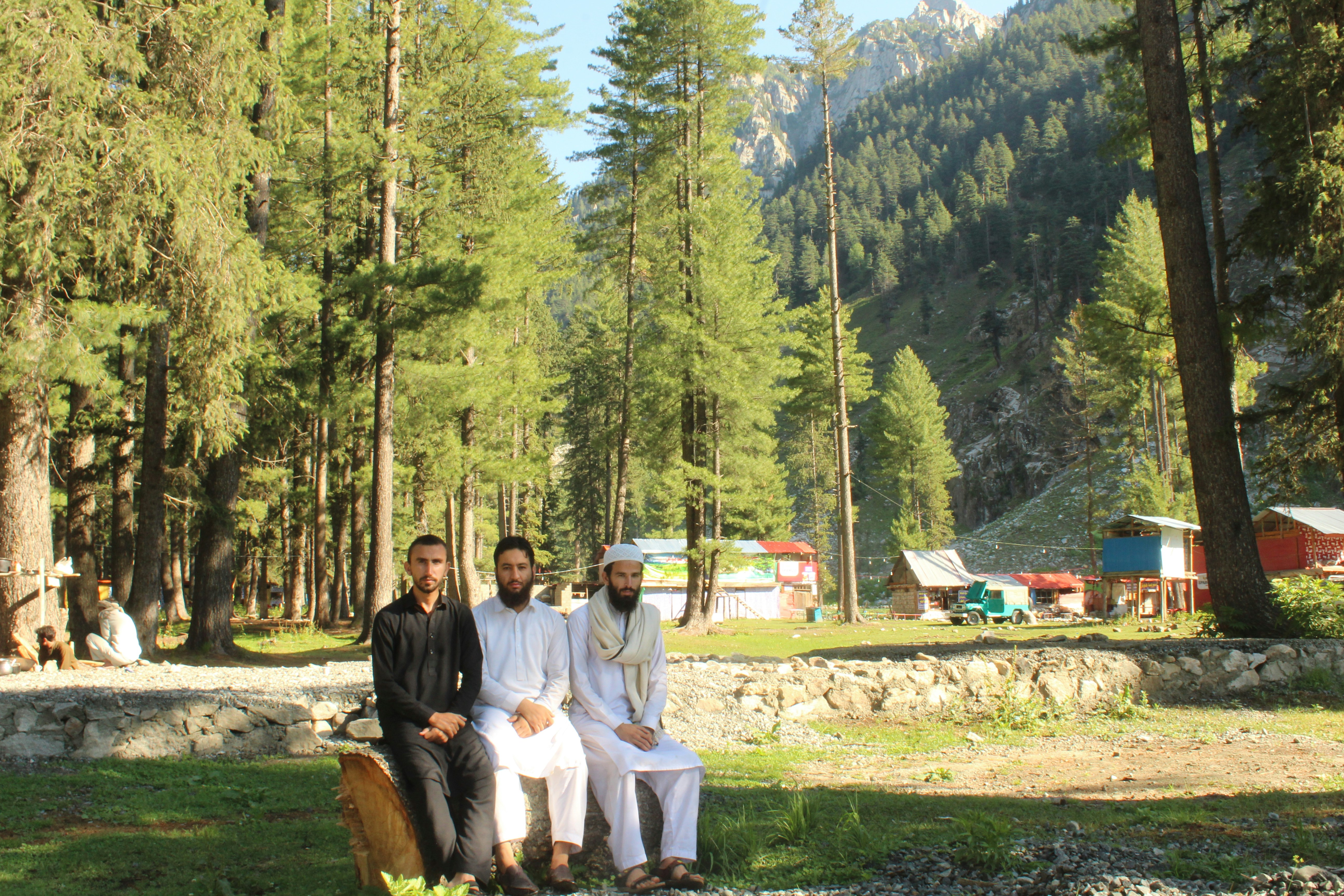 three men are sitting on a bench in the woods