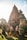 A traditional Balinese temple with intricate stone carvings is set against a bright sky. Two individuals dressed in ornate Balinese costume stand in front of the temple, posing elegantly. The lush greenery around them adds to the vibrant yet serene atmosphere.