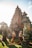 A traditional Balinese temple with intricate stone carvings is set against a bright sky. Two individuals dressed in ornate Balinese costume stand in front of the temple, posing elegantly. The lush greenery around them adds to the vibrant yet serene atmosphere.