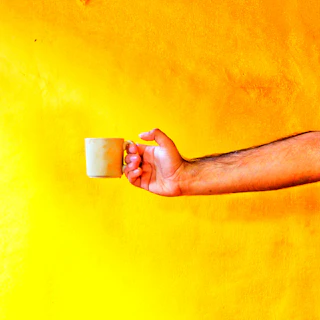 Hands holding a freshly glazed ceramic mug with a cheerful yellow hue.