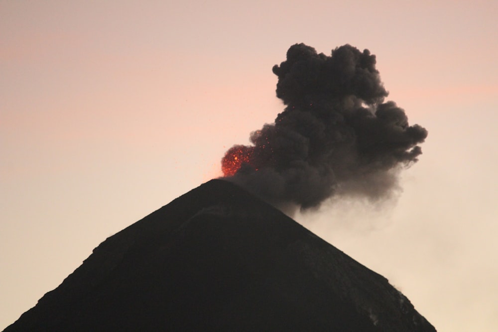 uma grande pluma de fumaça preta sai do topo de uma montanha