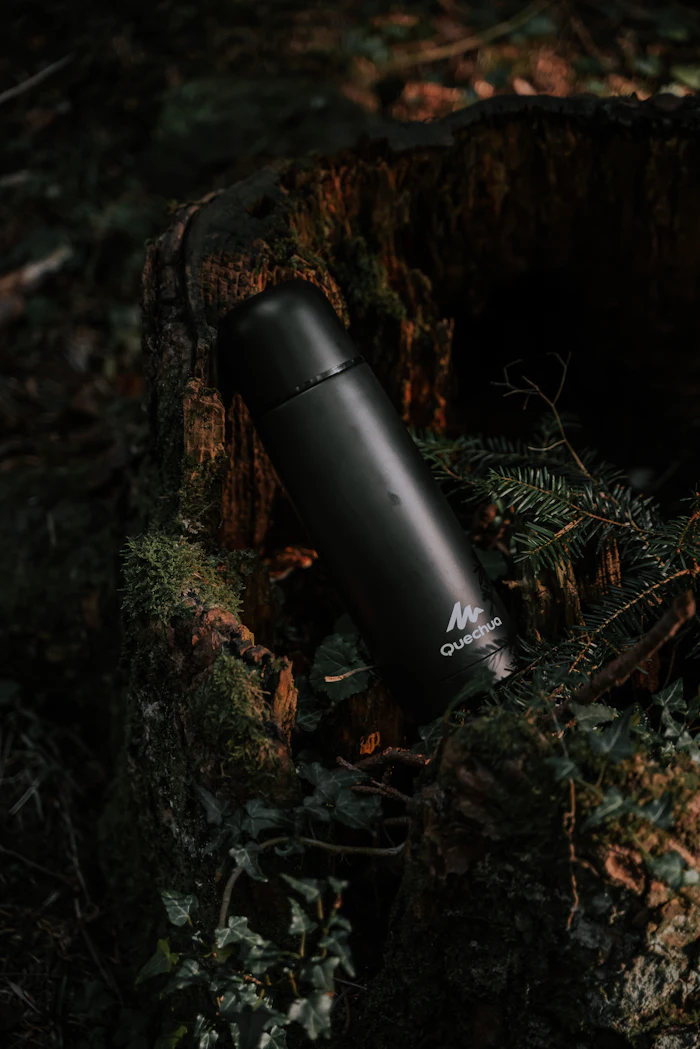 Botella térmica negra sobre un tronco en el bosque