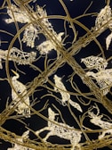 Intricate sculptures made of twinkling lights and metal wires are shaped like various animals, including birds and deer. The structures are intertwined in an elaborate circular pattern against a dark background, creating a mesmerizing and festive appearance.