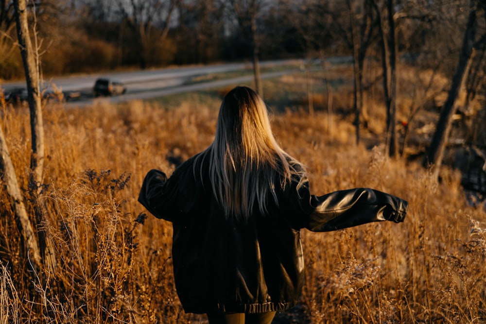 a woman with long hair walking through a field