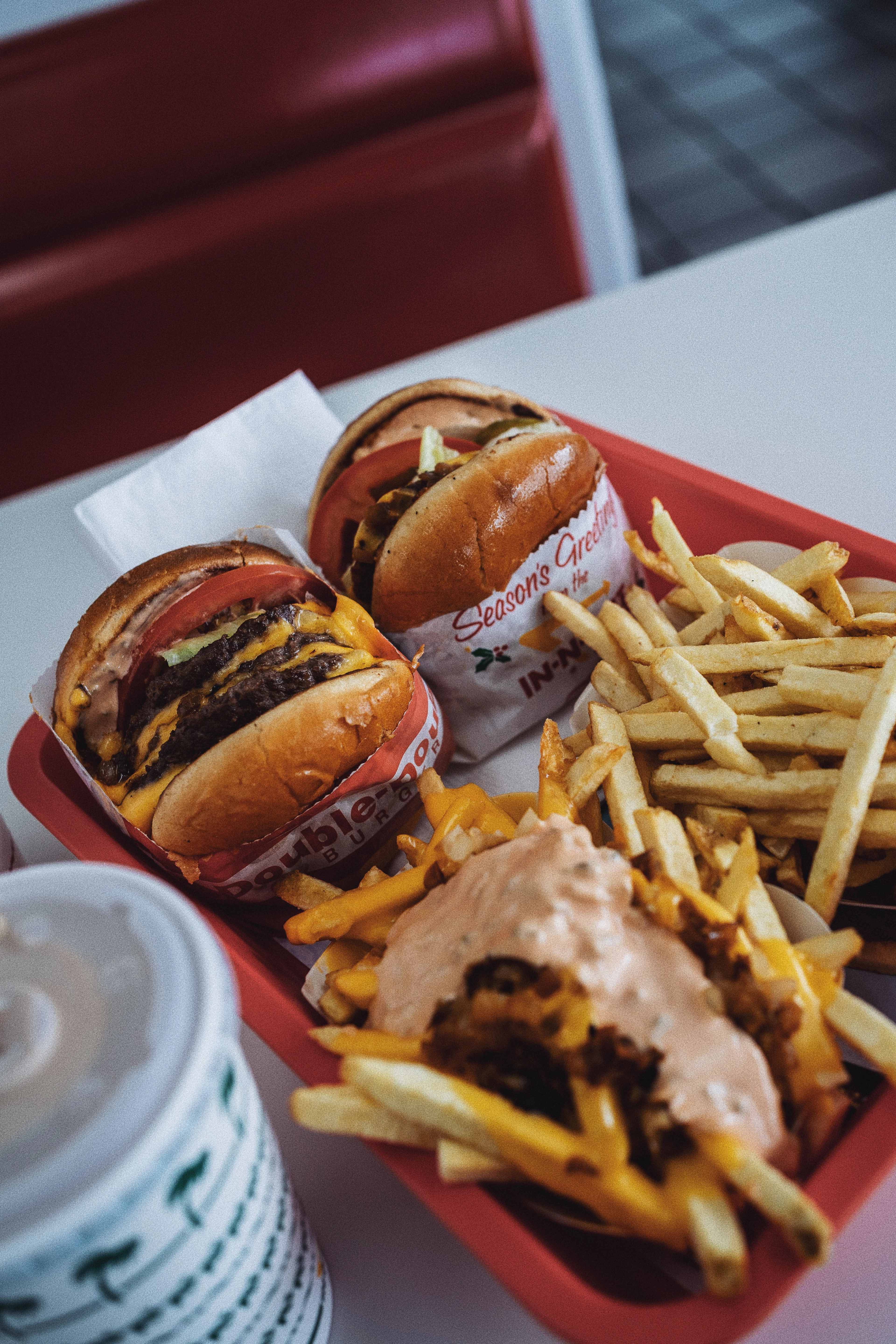 A red diner tray holding two cheeseburgers and a pile of fries smothered in melted cheese and pink burger sauce, on a table in a red vinyl booth in Las Vegas