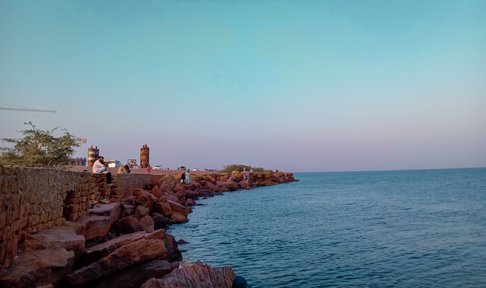 a group of people standing on top of a stone wall next to the ocean