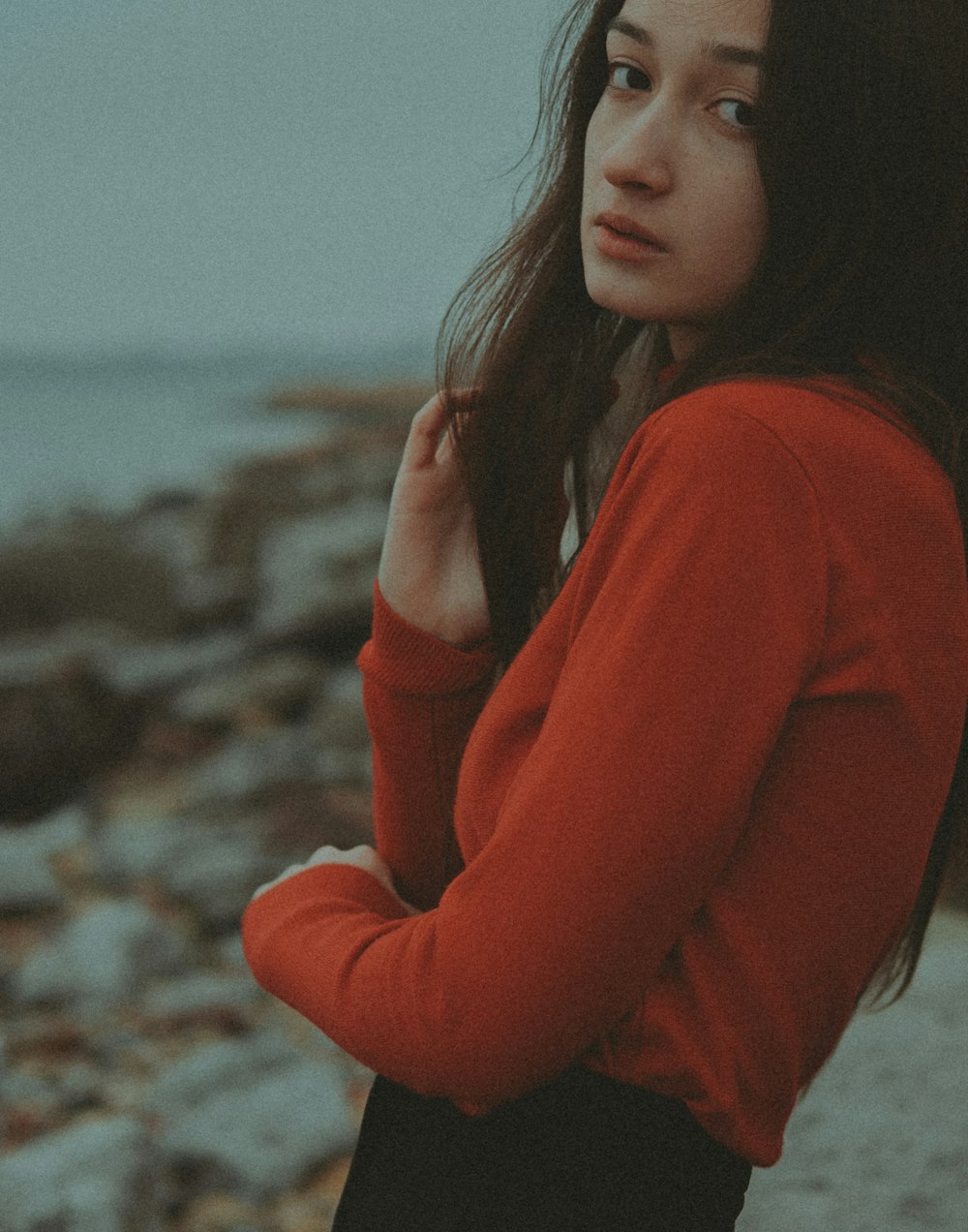 a woman in a red sweater standing on a rocky beach