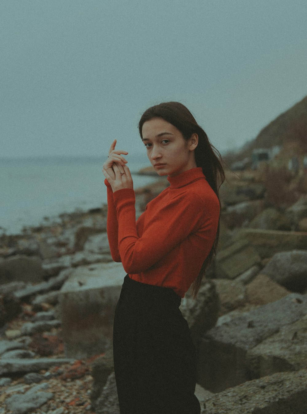 a woman standing on a rocky beach smoking a cigarette