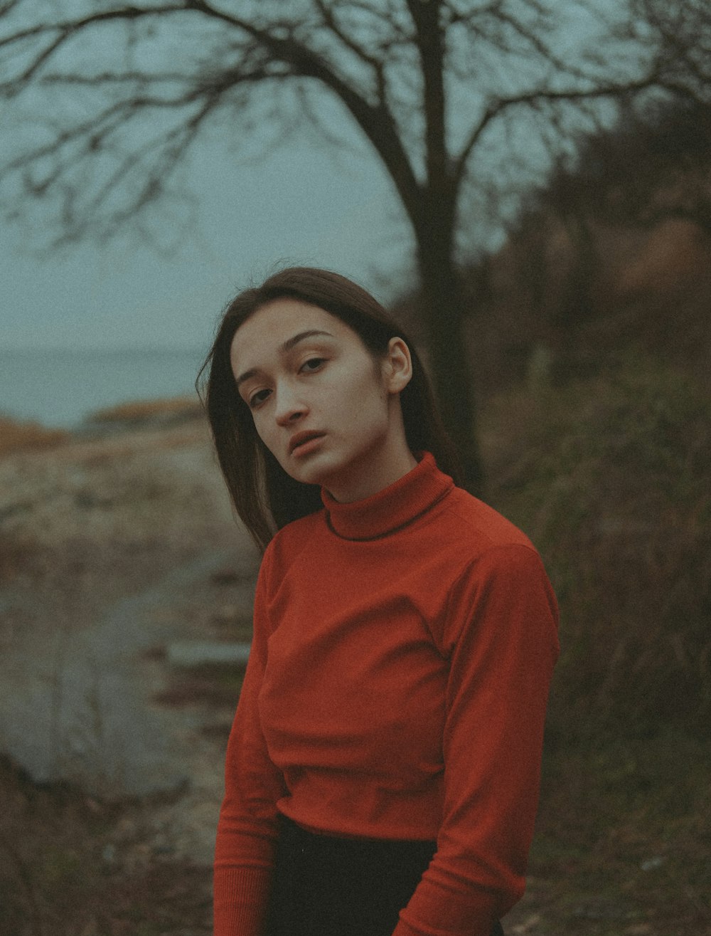 a woman in a red shirt is standing near a tree