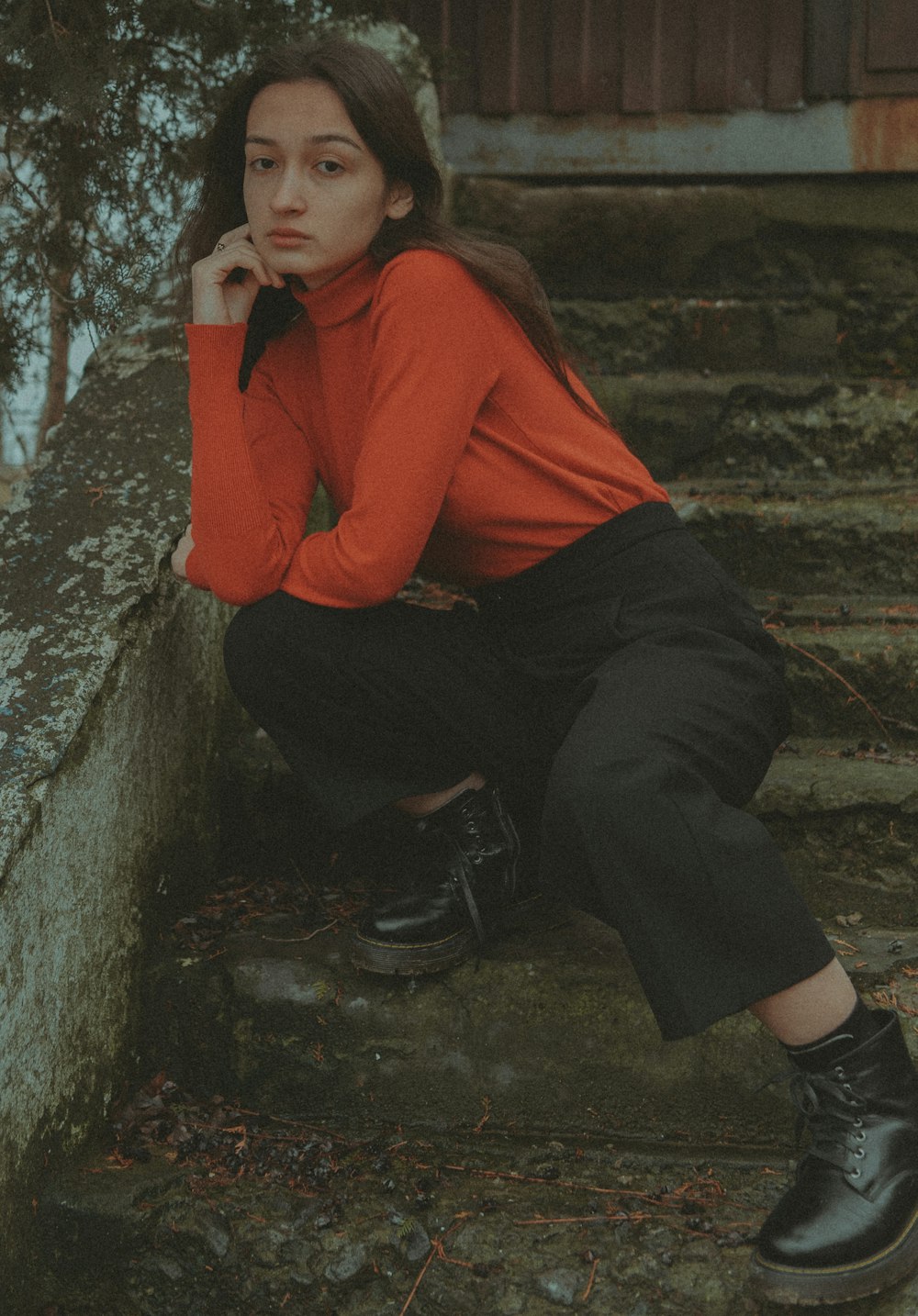 a woman in a red shirt and black pants sitting on steps