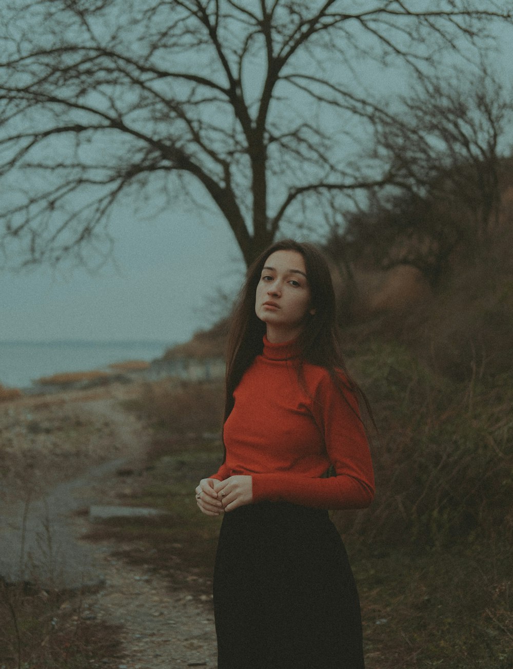 a woman in a red top is standing by a tree