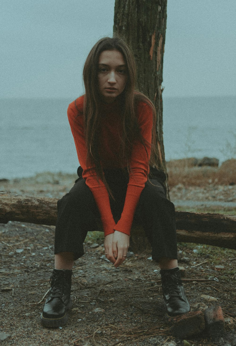 a woman in a red shirt and black pants sitting on a log