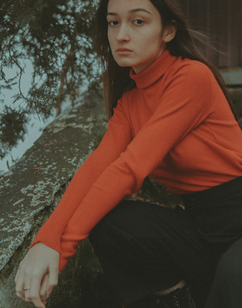 a woman in a red shirt is sitting on a rock
