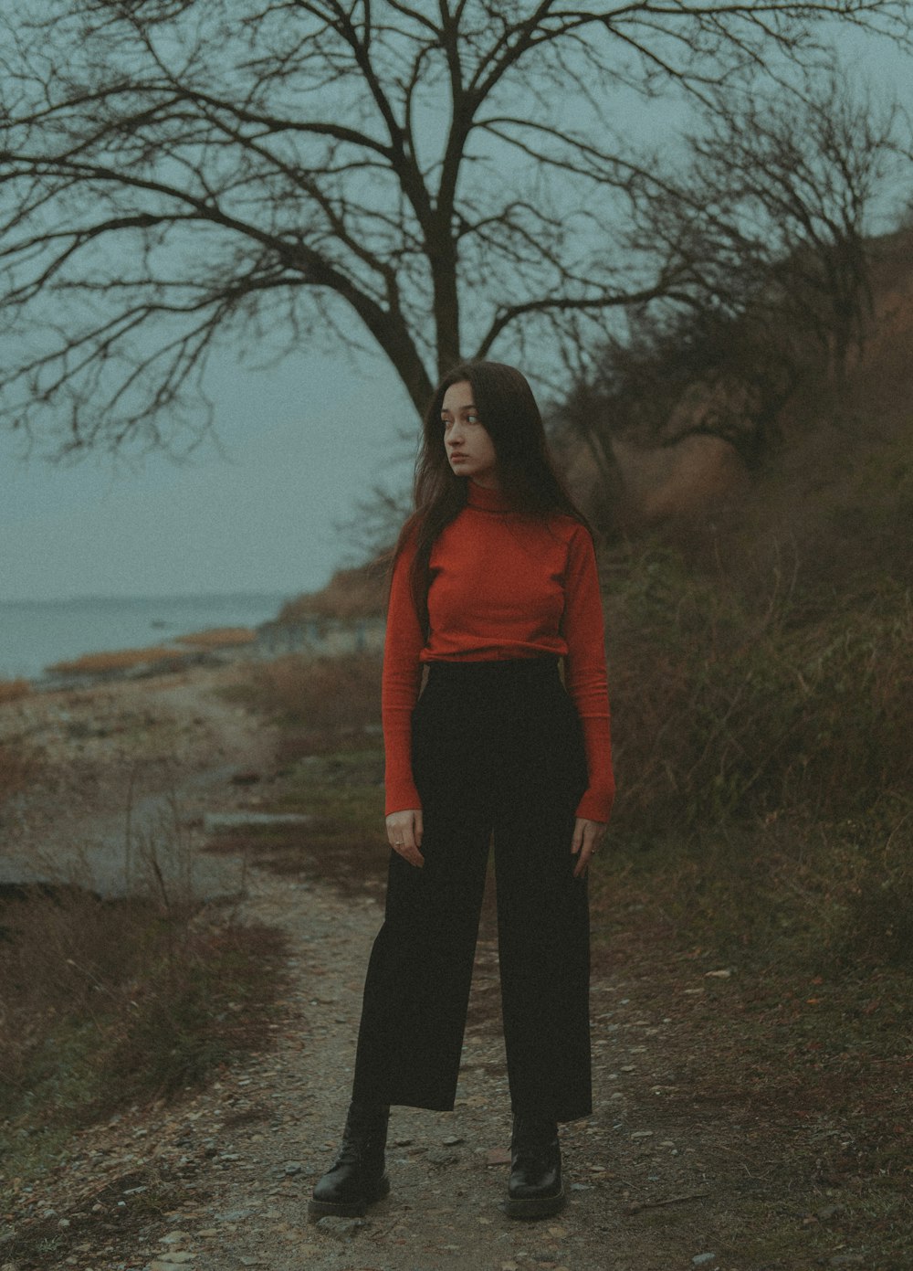 a woman standing on a dirt road next to a tree