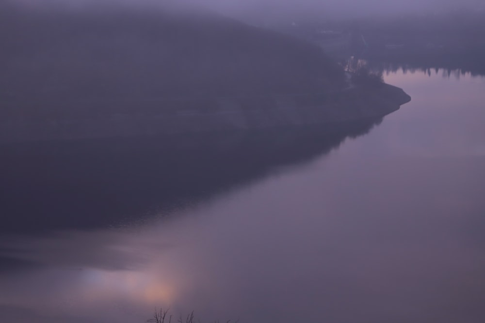 a body of water surrounded by fog and trees