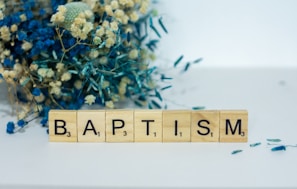 a wooden block spelling baptism next to a bouquet of flowers