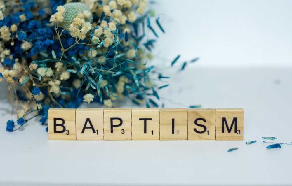 a wooden block spelling baptism next to a bouquet of flowers