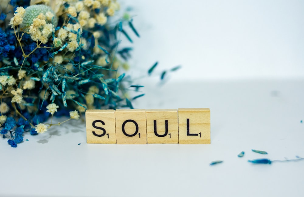 Un blocco di legno che scandisce la parola anima accanto a un mazzo di fiori