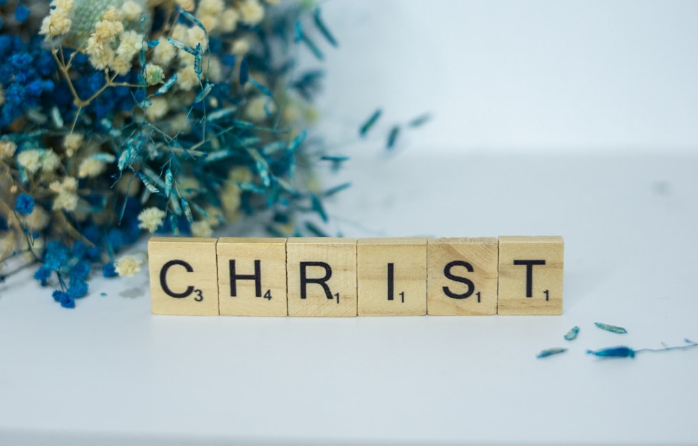 a wooden block that says christ next to a bouquet of flowers