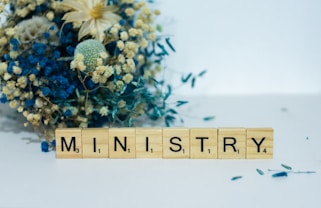 a scrabble block spelling the word mn, in front of a bouquet of