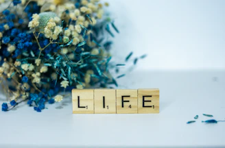 a wooden block that says life next to a bouquet of flowers