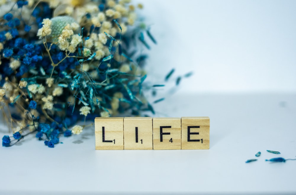 a wooden block that says life next to a bouquet of flowers
