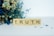 Wooden Scrabble tiles spell out the word 'TRUTH', placed on a surface with a background of dried flowers, including blue and beige tones.