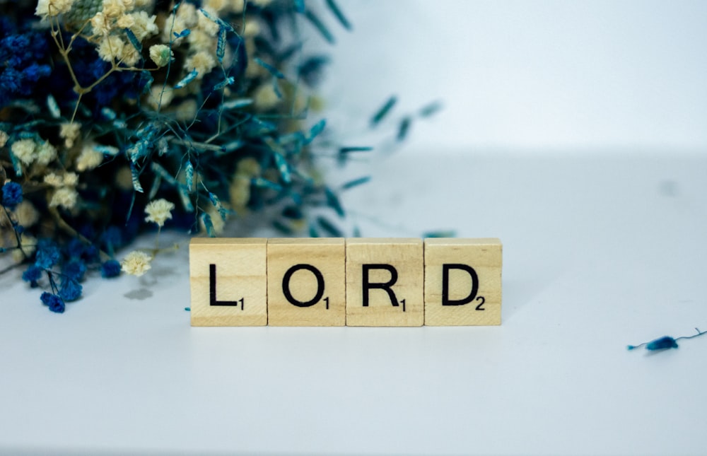 a scrabble block spelling the word lord next to a bouquet of flowers