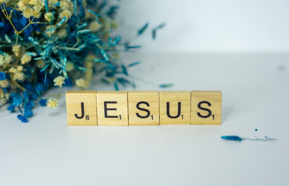 a wooden block spelling jesus next to a bouquet of flowers