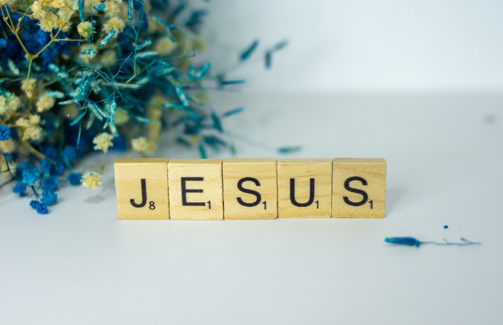 Un blocco di legno che scrive Gesù accanto a un mazzo di fiori