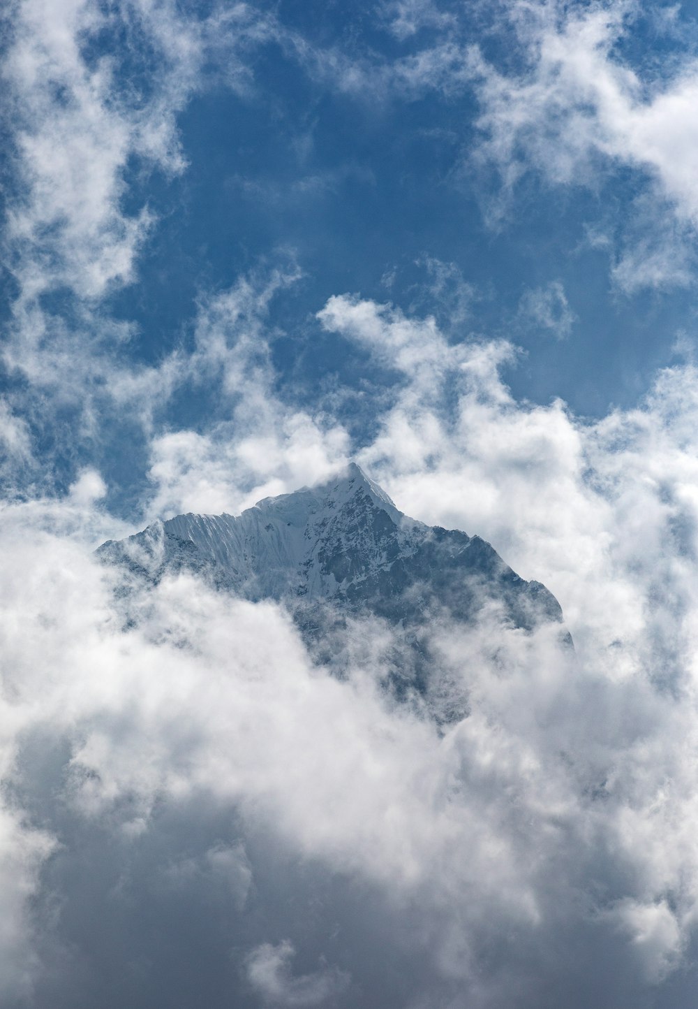 a large mountain covered in clouds under a blue sky