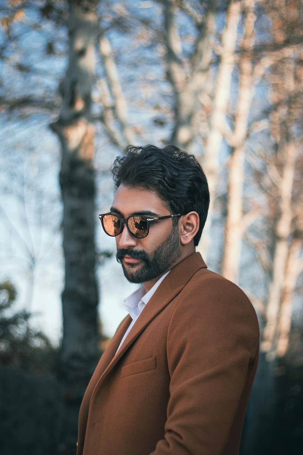 a man in a suit and sunglasses standing in front of a tree