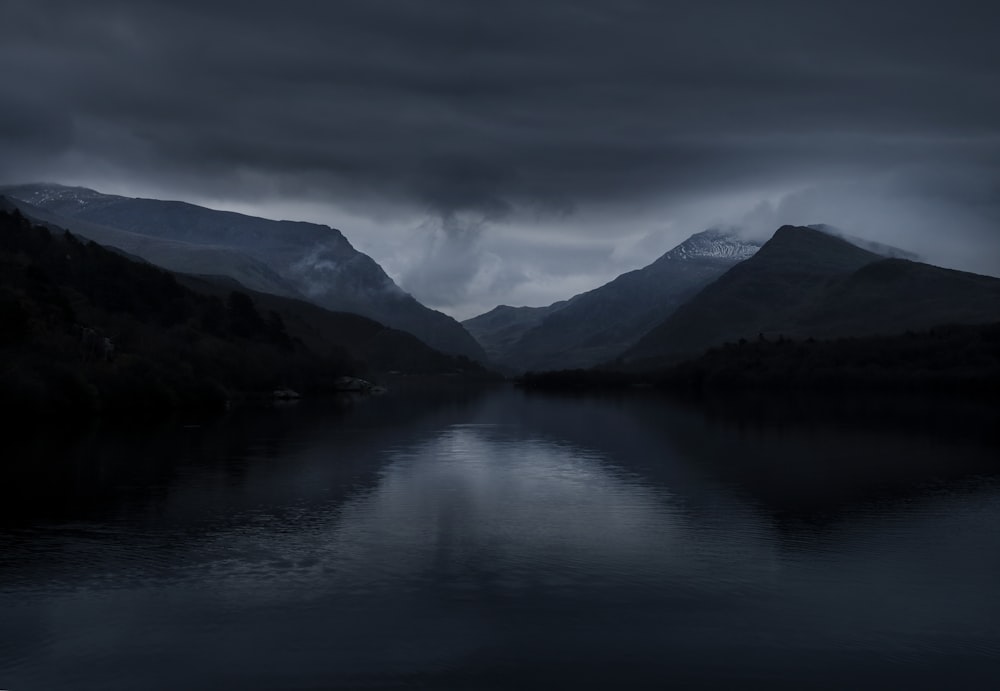 a body of water surrounded by mountains under a cloudy sky