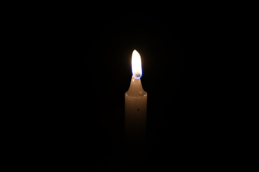 a lit candle in the dark with a black background