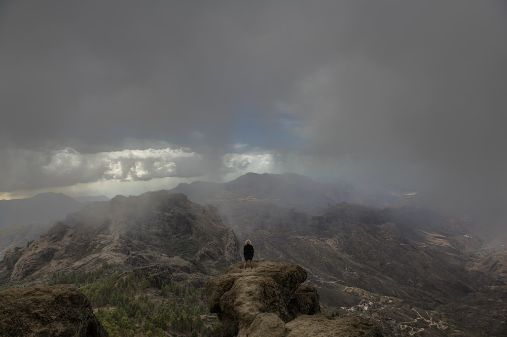 uma pessoa de pé no topo de uma montanha sob um céu nublado