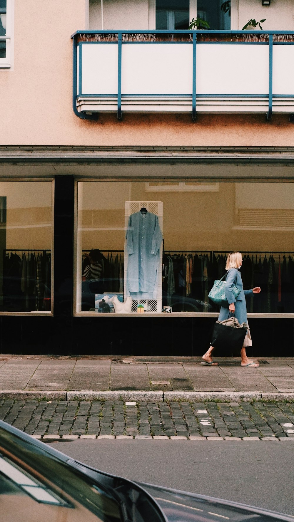 a woman walking down a street past a clothing store