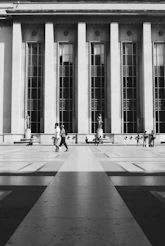 a black and white photo of people walking in front of a building