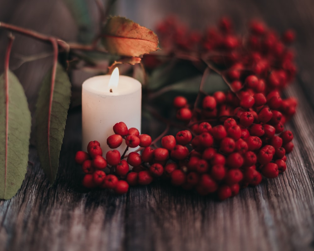 a white candle surrounded by red berries and leaves