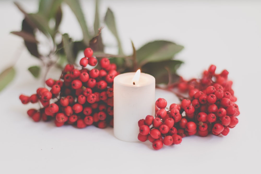 a white candle surrounded by red berries and greenery