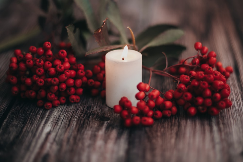 a candle surrounded by berries on a wooden table