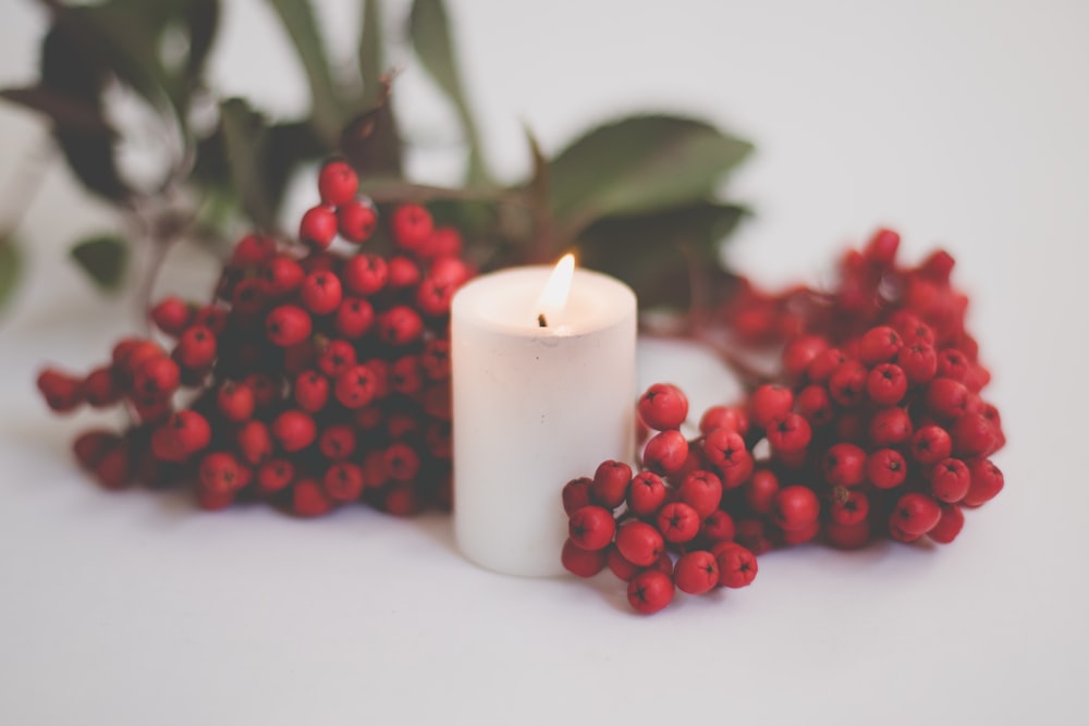 a white candle surrounded by red berries
