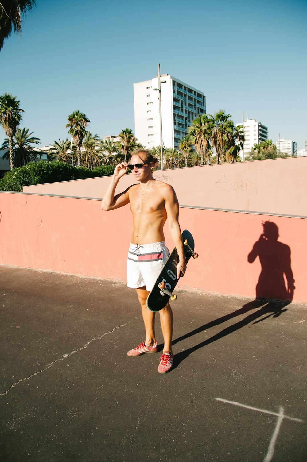 a shirtless man holding a skateboard in a parking lot