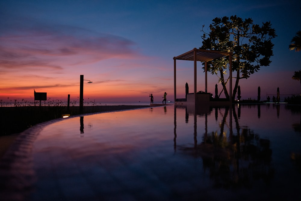 a pool with a gazebo and a sunset in the background