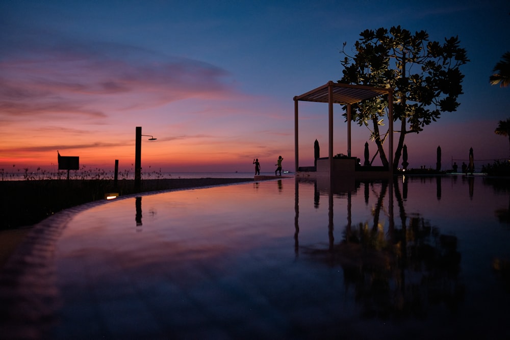 uma piscina com um gazebo e um pôr do sol ao fundo