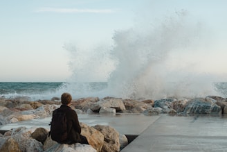 a person sitting on a rock near the ocean
