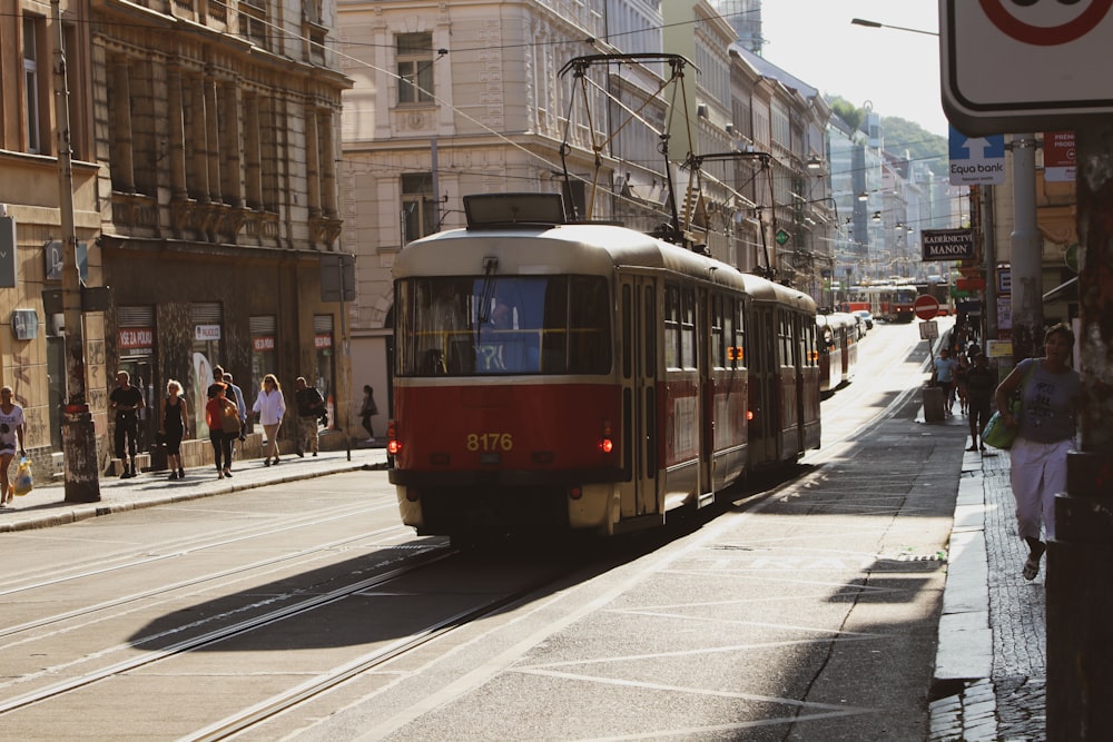 a red and white train traveling down a street next to tall buildings