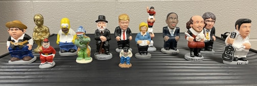 A collection of small, colorful figurines depicting various pop culture and historical characters are arranged in two rows on a flat surface. Each figurine is uniquely styled to represent their iconic features.