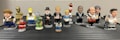 A collection of small, colorful figurines depicting various pop culture and historical characters are arranged in two rows on a flat surface. Each figurine is uniquely styled to represent their iconic features.